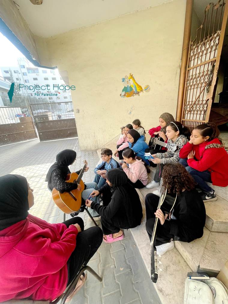Children gathered around a guitarist at a Project Hope music session