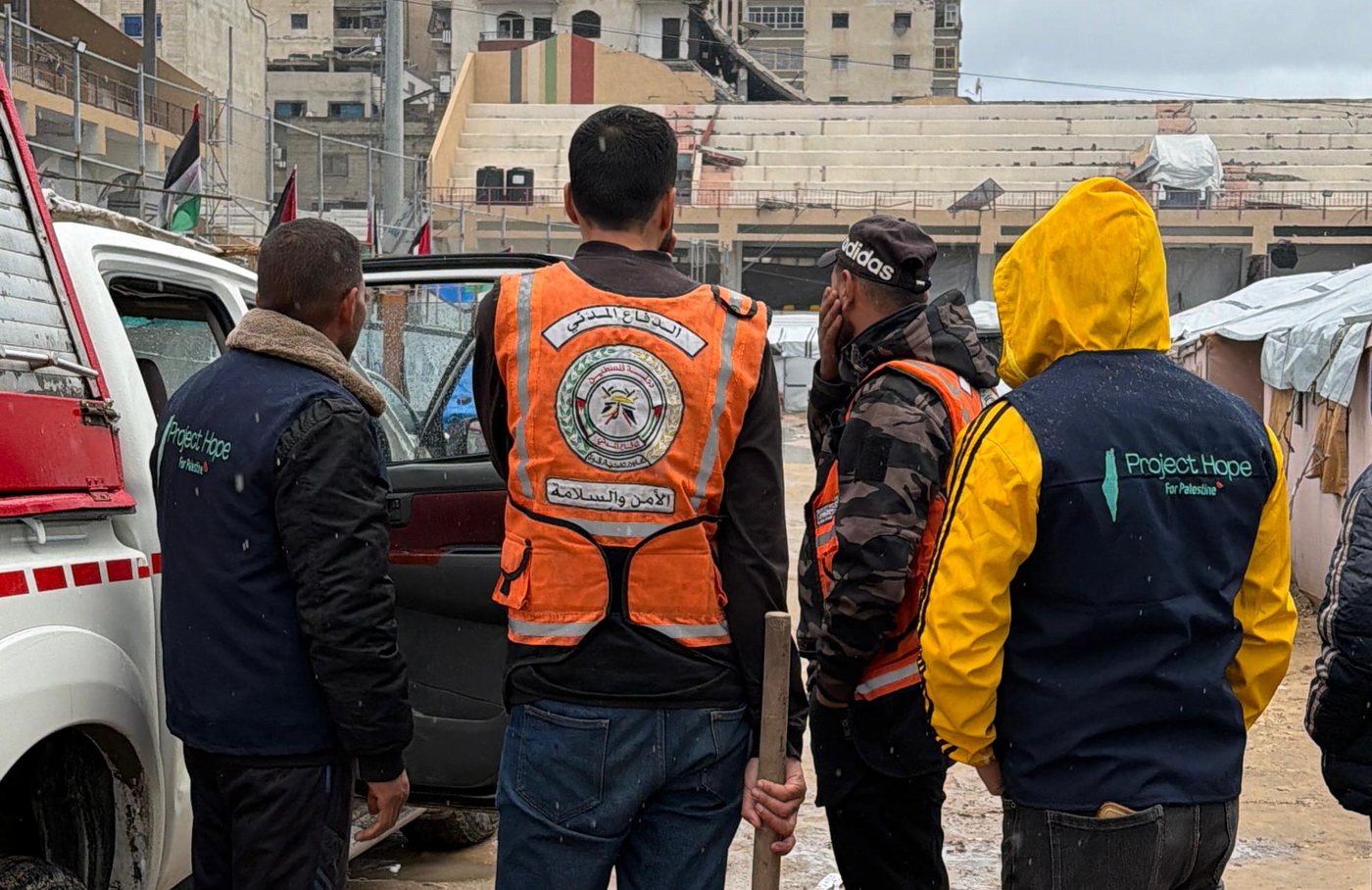Project Hope volunteers standing with a Palestinian Civil Defense crew beside a vehicle in a Gaza displacement camp