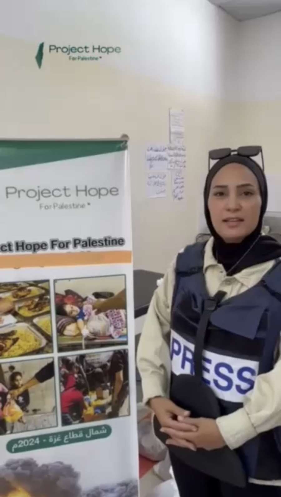 A Palestinian journalist in a press vest beside a Project Hope banner